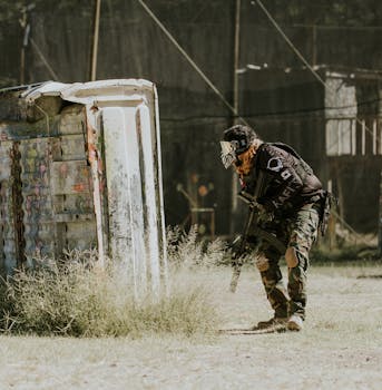 A player in tactical gear strategizes during a high-energy outdoor paintball match.