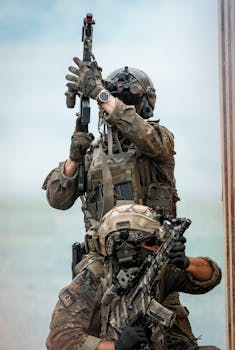 Two soldiers in camouflage gear focus during a military training exercise, armed with rifles.